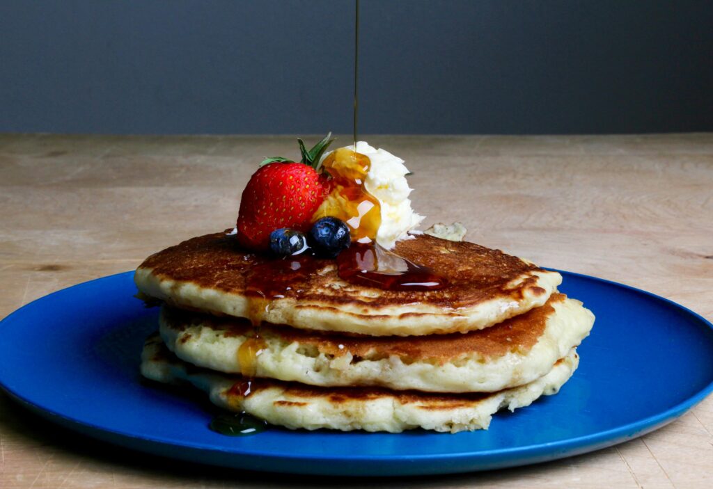 pexels-photo-718739-718739 Stack of fluffy pancakes topped with syrup, strawberries, blueberries, and cream on a blue plate.
